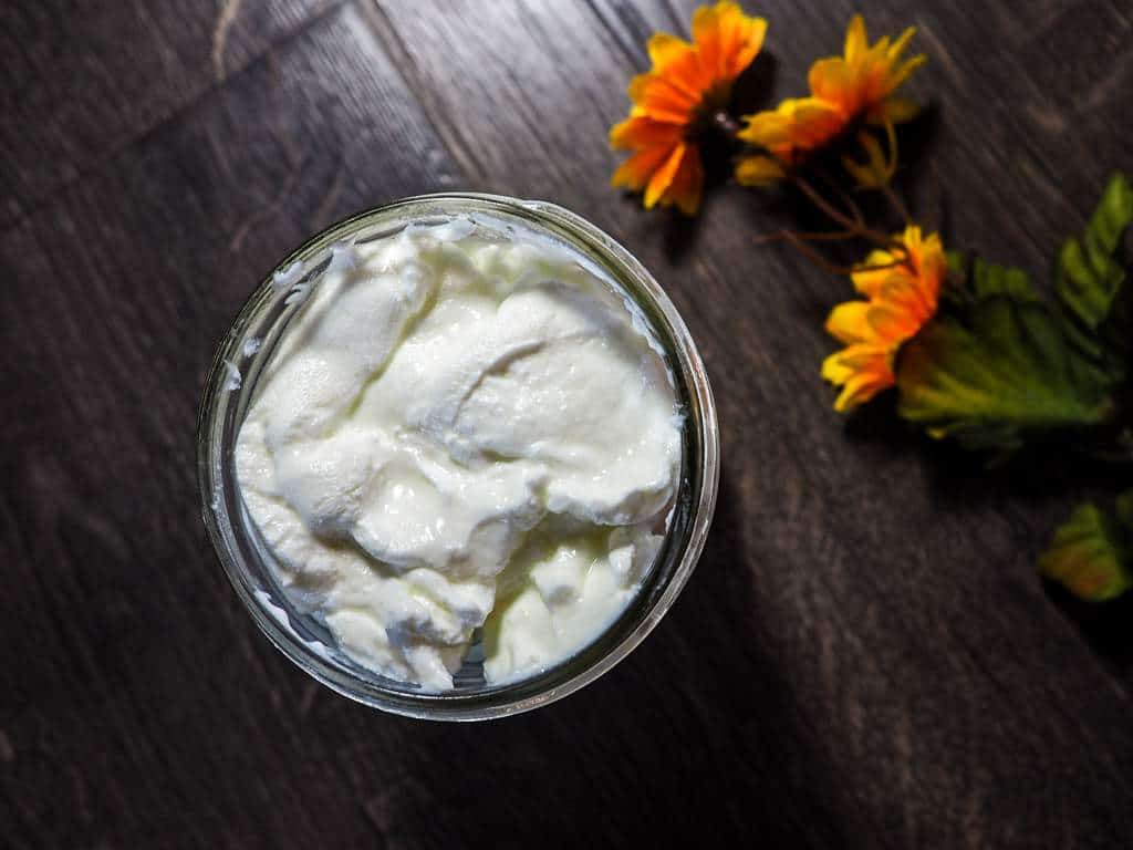 A mason jar full of homemade yogurt and a yellow flower on a gray wood background.