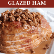 A pin image of a sliced ham on a white plate with maple, bourbon, and pecan glaze drizzled over the top of it.