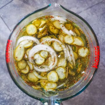 A large pyrex measuring cup with pickles and onions in a brine in it.