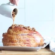 A sliced ham with bourbon pecan glaze being poured over it.