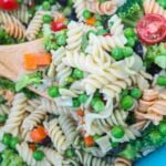 A bowl of pasta salad and a wooden spoon, zoomed in.