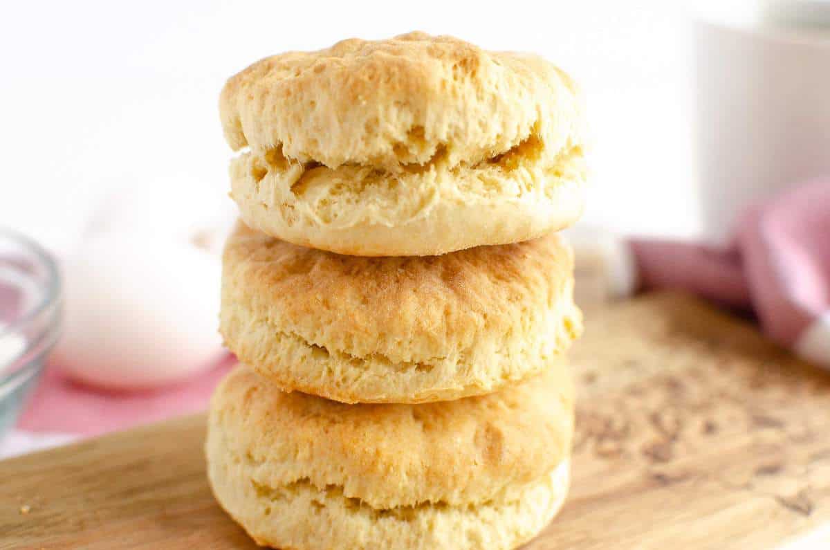 A stack of 3 sour cream biscuits on a wood cutting board.