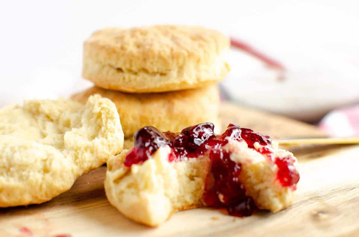 A pile of biscuits with jelly on one of them on a wood board.