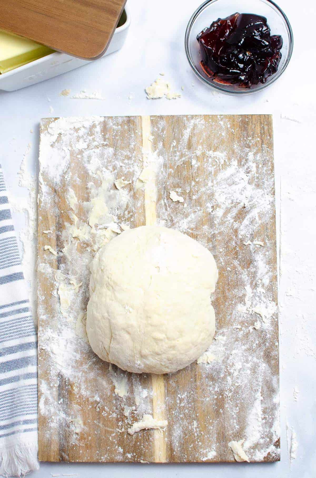 A ball of biscuit dough on a wood cutting board.