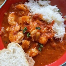 A red bowl of shrimp creole with rice and french bread.
