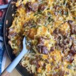 A skillet with cheesy hash brown breakfast casserole with a gray spoon.