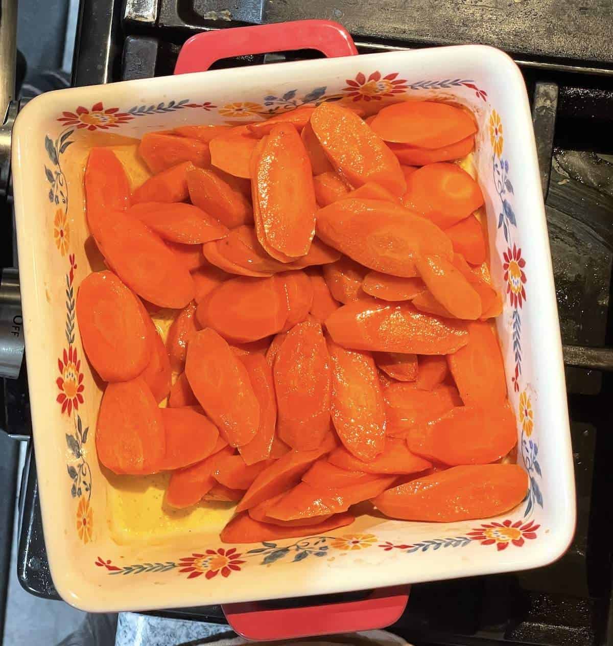 A flowery square baking dish filled with butter roasted carrots fresh from the oven.