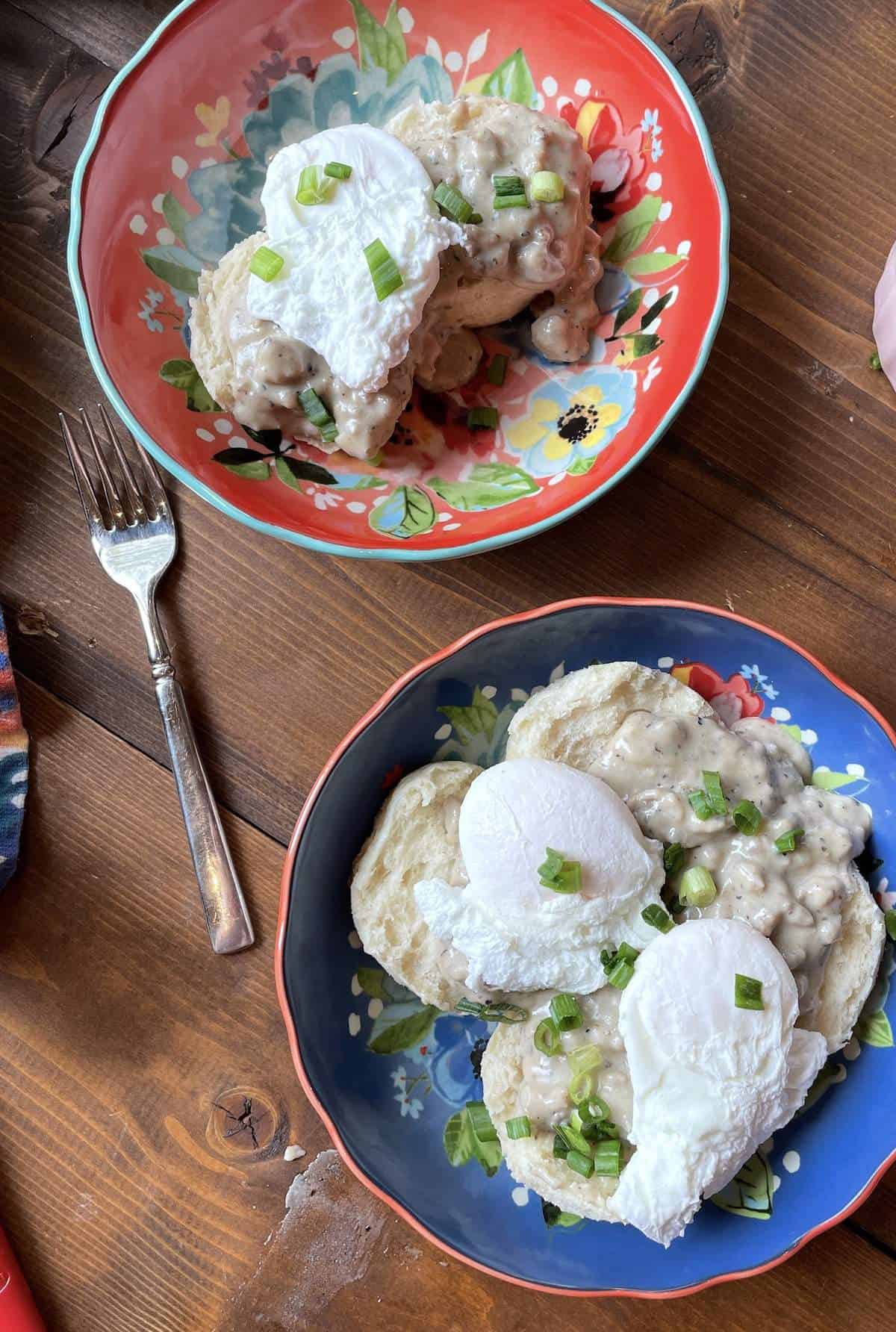 Two bowls with two biscuits topped with sausage gravy and two poached eggs.