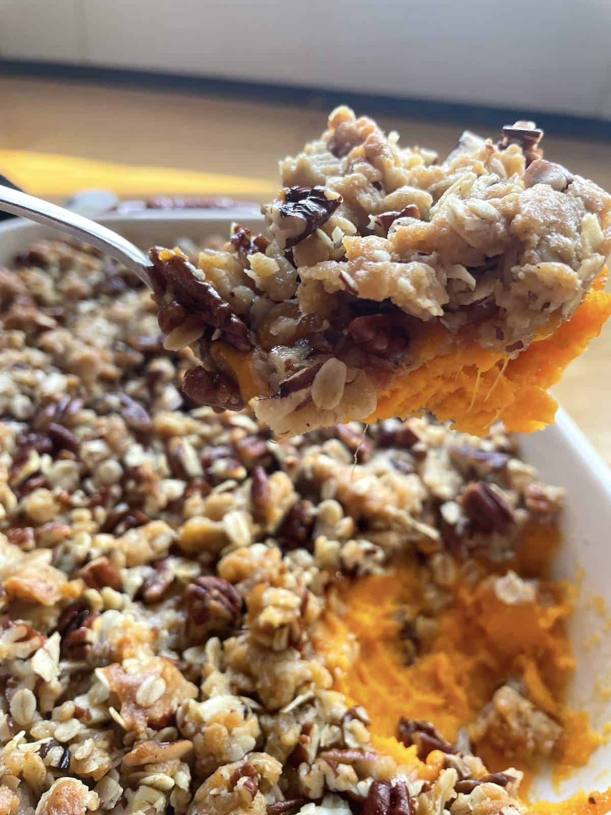 A pan of sweet potato casserole with praline topping with a scoop held above it.