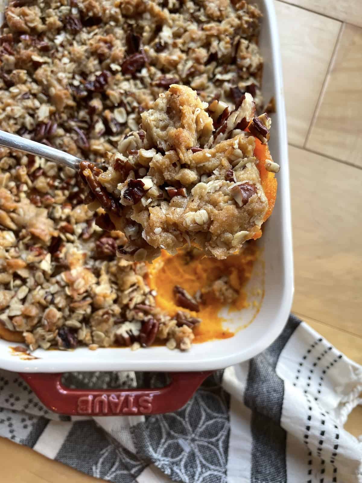 A pan of sweet potato casserole with praline topping with a scoop held above it.
