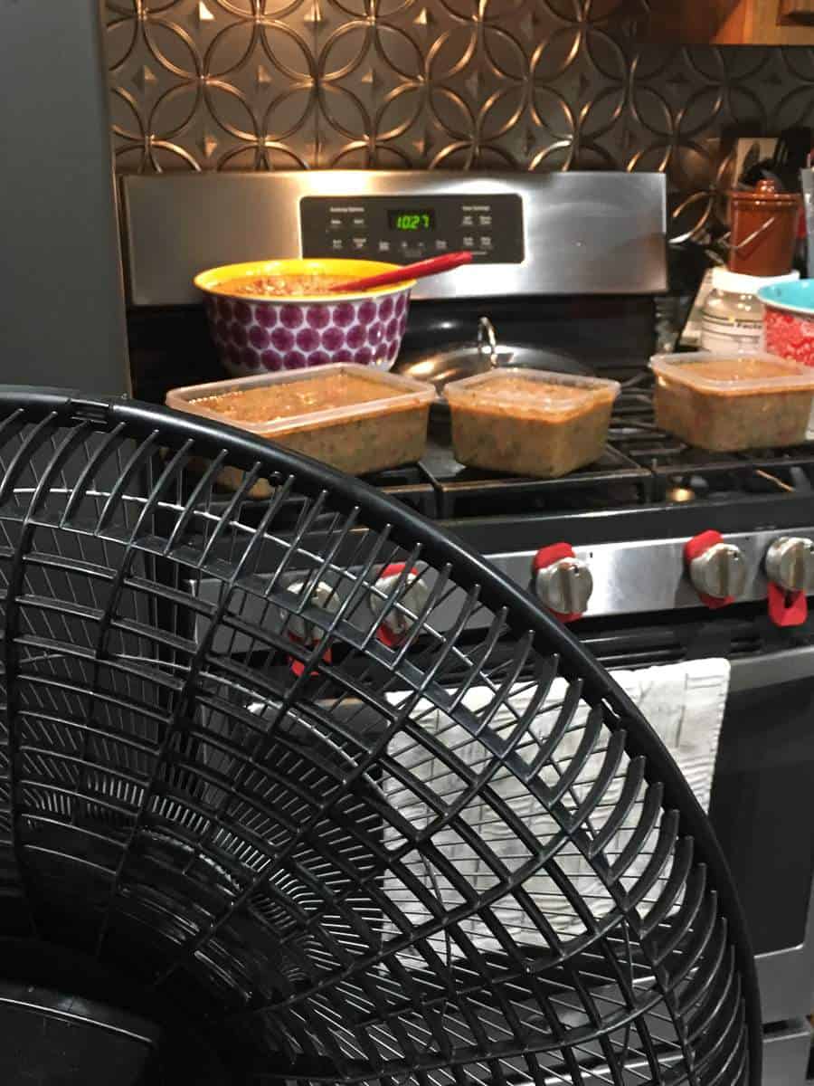 Containers of gumbo cooling on the stove with a fan blowing at them.