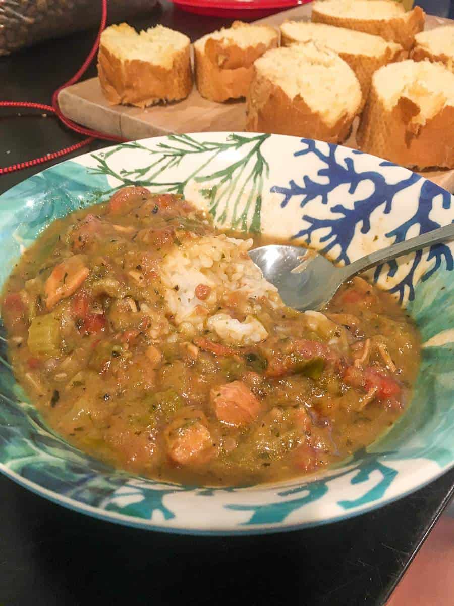 A bowl of chicken and sausage gumbo with a plate of french bread behind it.