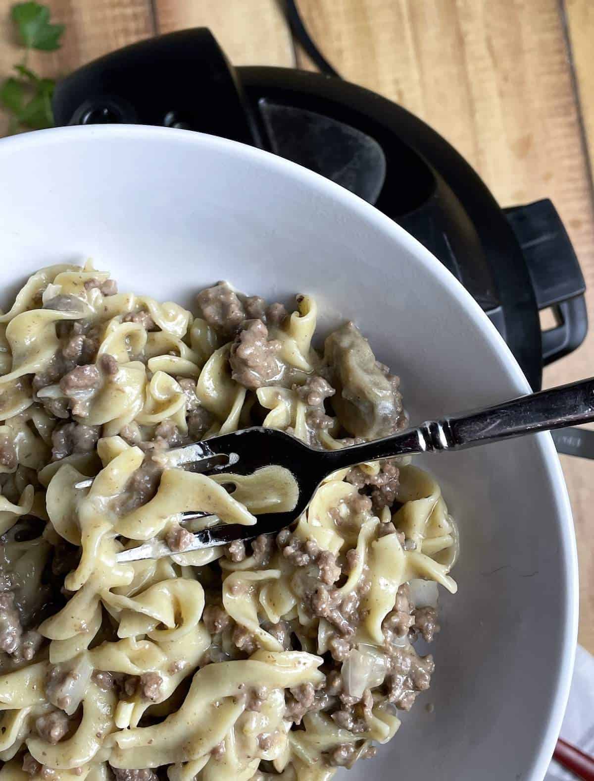 Instant Pot Ground Beef Stroganoff in a white bowl held over an Instant Pot.
