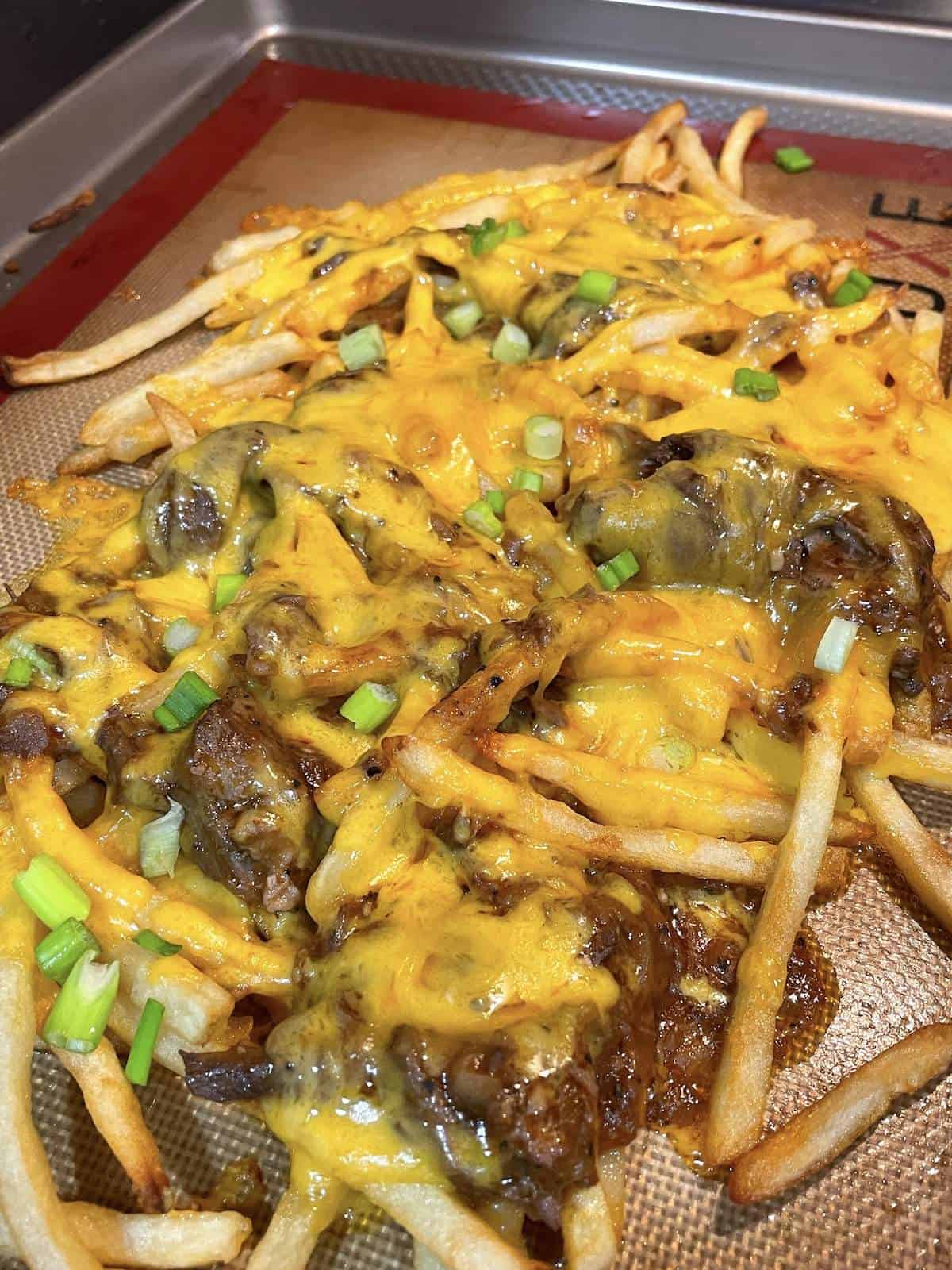 A baking sheet with French fries topped in roast beef debris with cheese on top.