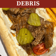 A pin image of a roast beef debris po'boy on French bread with lettuce, tomato, and pickles and French fries on the side.