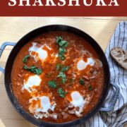 A pin image of a pan of creole tomato shakshuka with 5 eggs and sourdough bread next to it.
