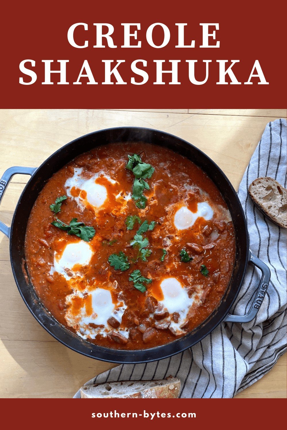 A pin image of a pan of creole tomato shakshuka with 5 eggs and sourdough bread next to it.