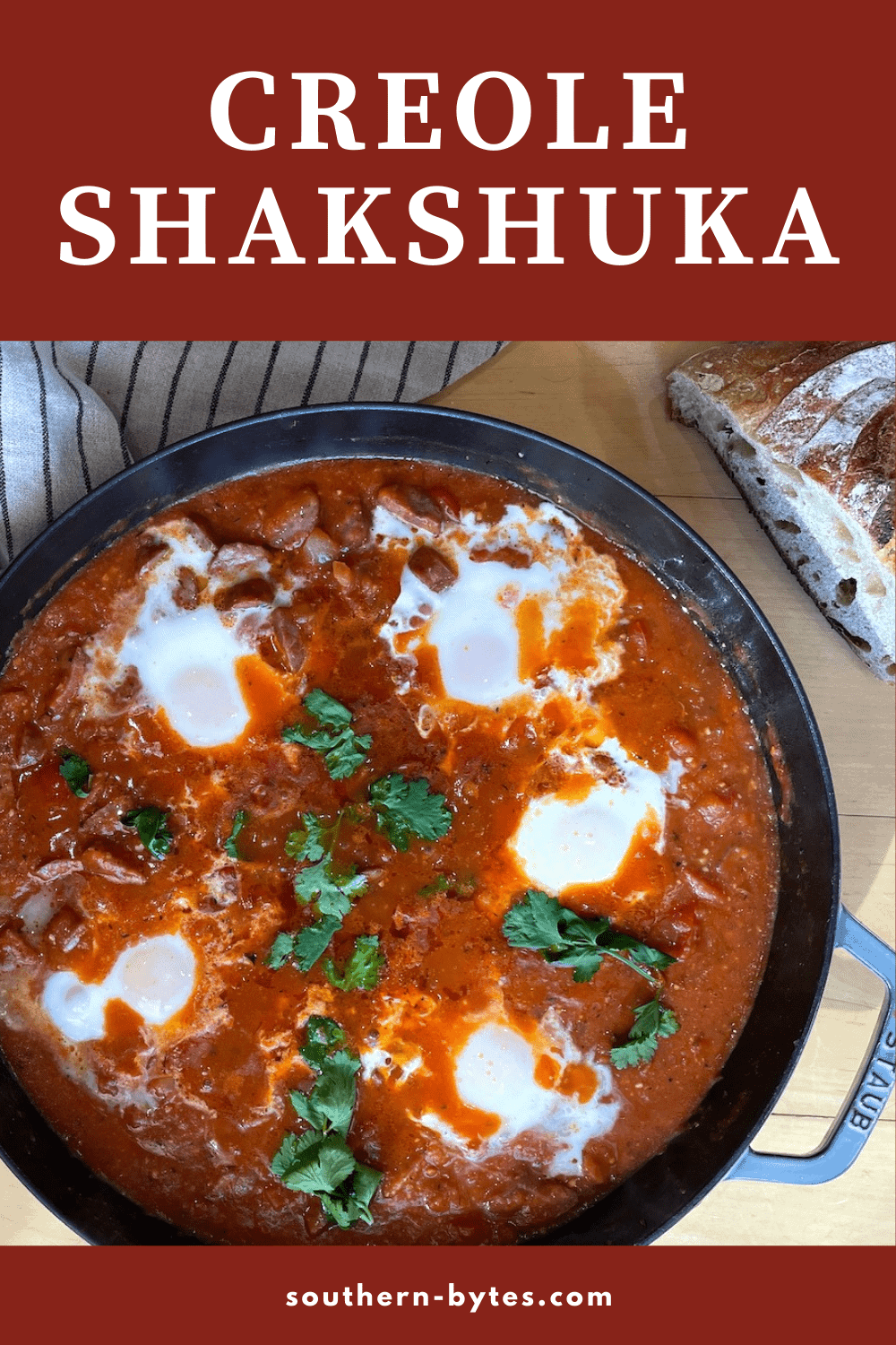 A pin image of a pan of creole tomato shakshuka with 5 eggs and sourdough bread next to it.