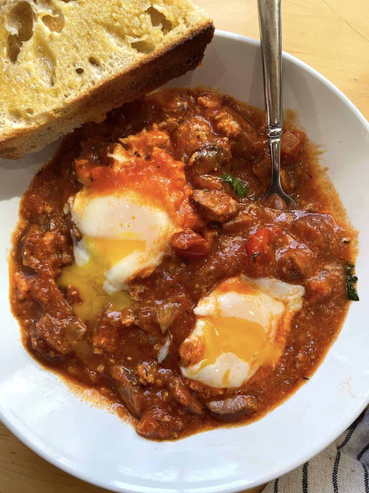 A bowl of creole shakshuka with two runny eggs in it.