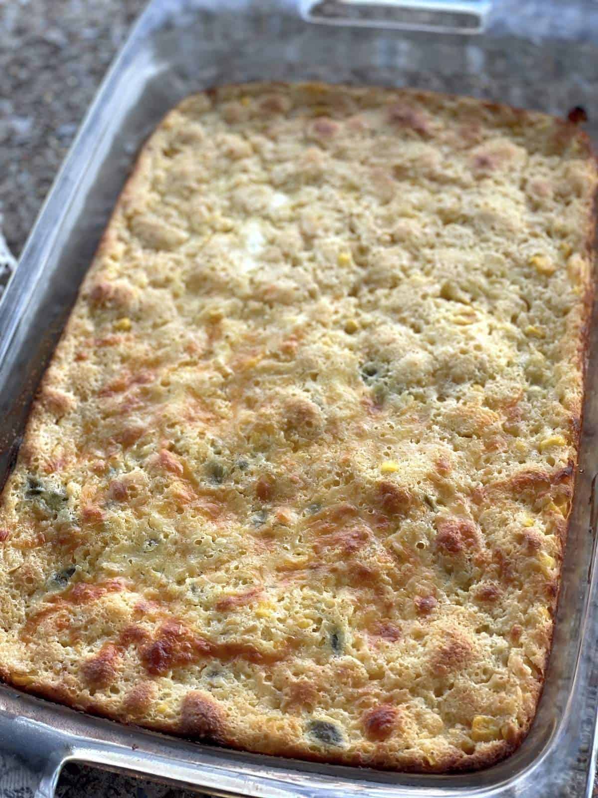 A pan of corn pudding, half with cheese and jalapeños in it.
