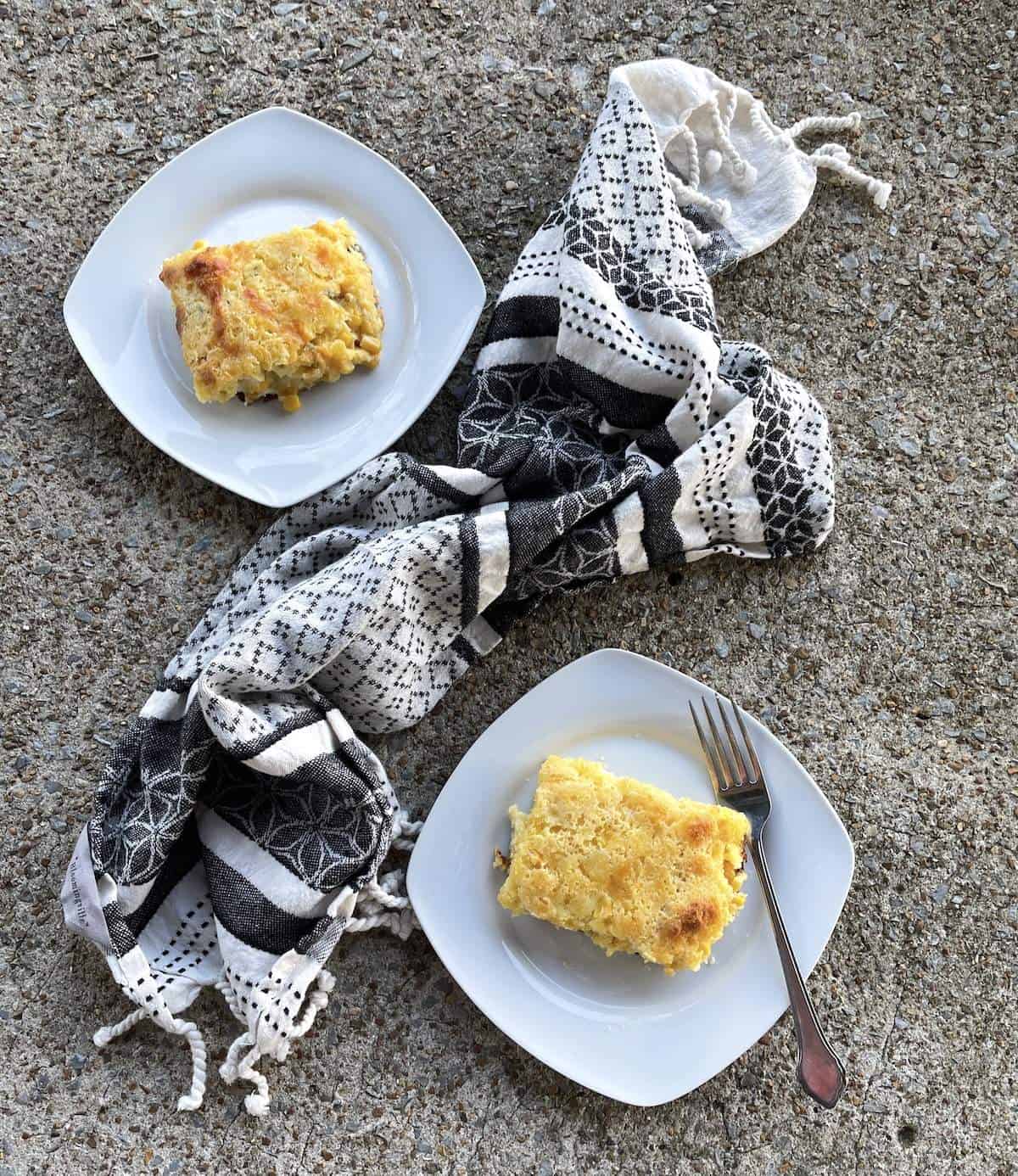 Two white plates with a square of corn pudding on each one and a tea towel.