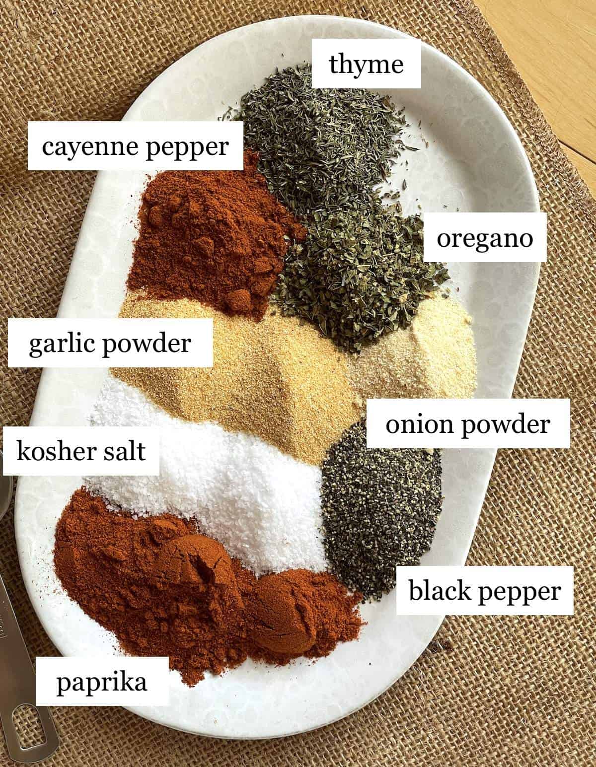 The ingredients in homemade cajun seasoning on a plate, laid out and labeled.