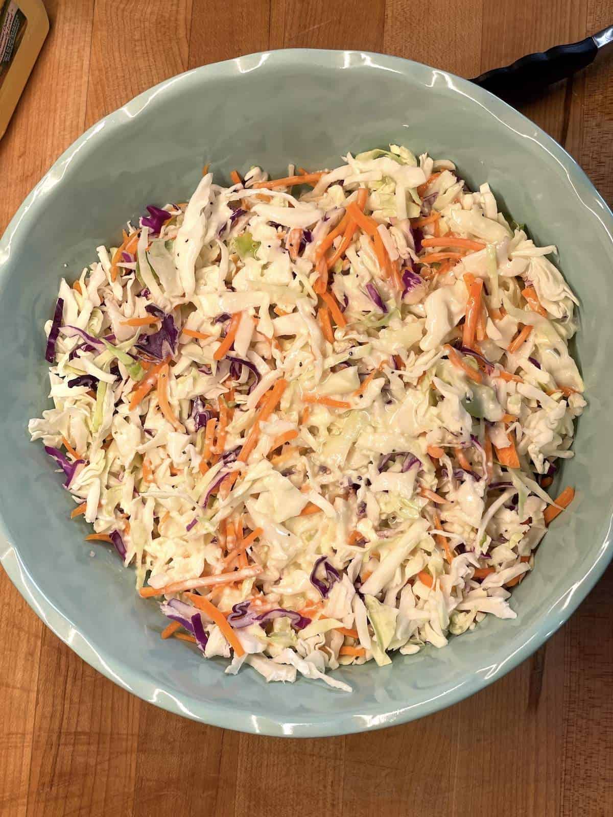 A bowl of shredded cabbage drizzled in coleslaw dressing.