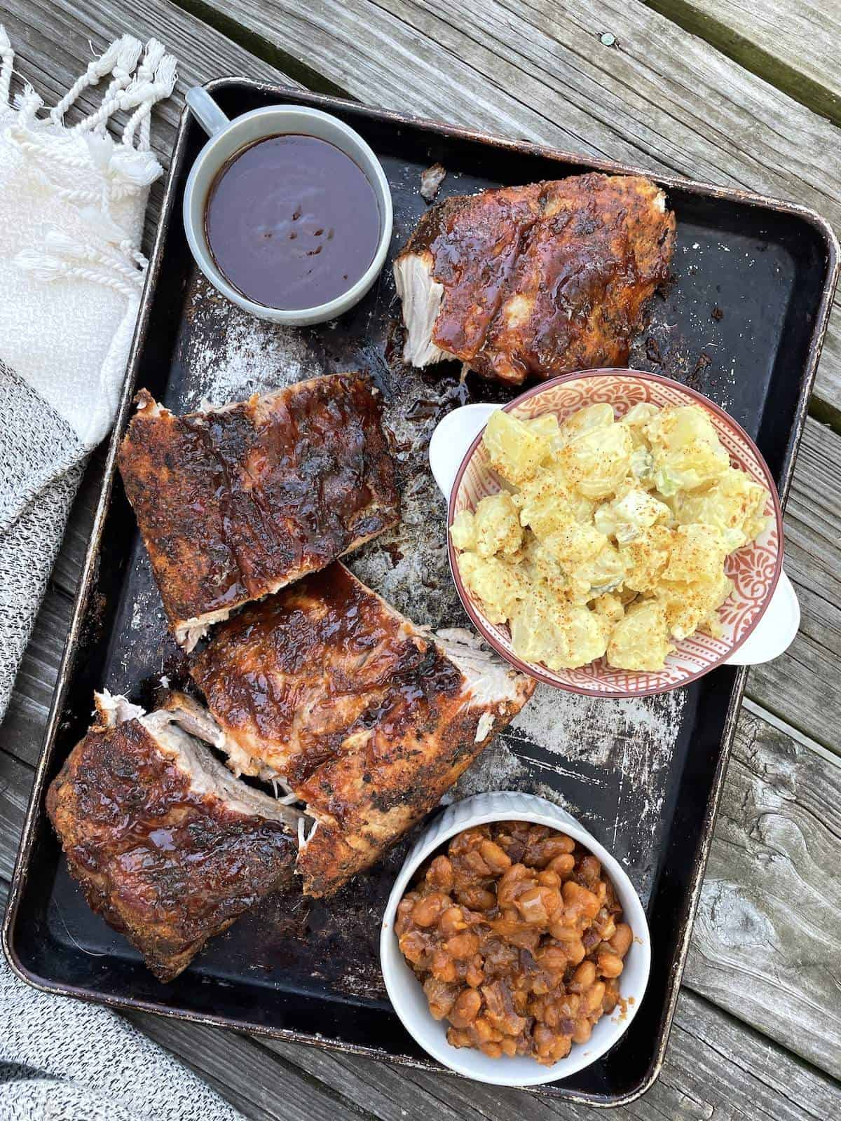 A tray with baked beans from scratch, baby back ribs, and southern potato salad.