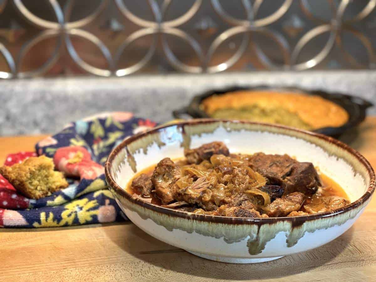 A bowl of country style ribs with a dish of cornbread behind it.