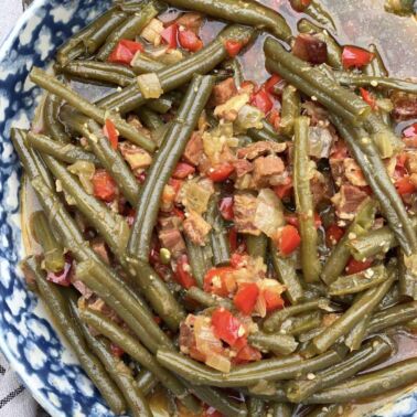 A bowl of southern style green beans cooked in a crock pot with ham, bacon, and red bell peppers.