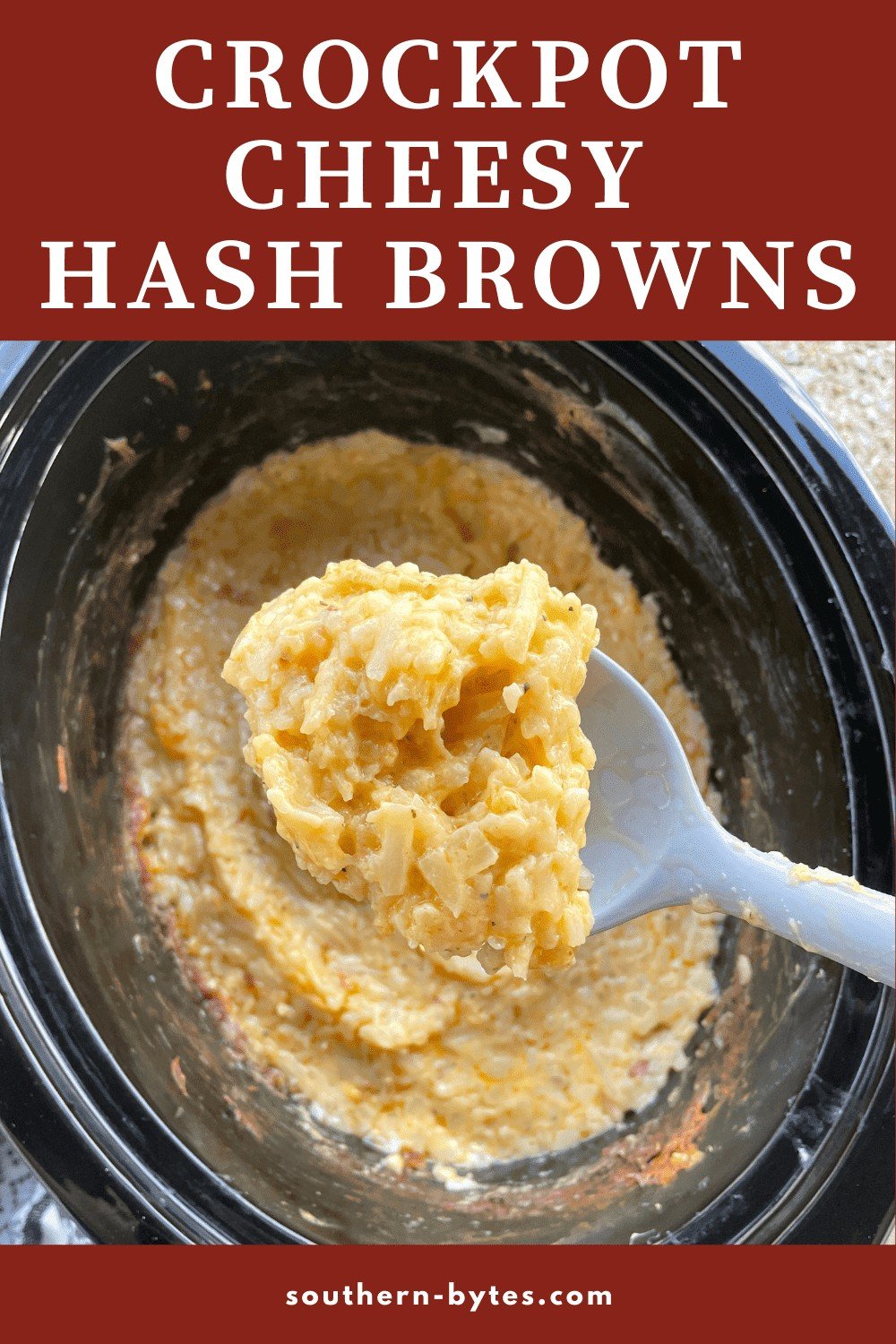 A pin image of a spoon of crockpot cheesy hash browns over a crockpot.