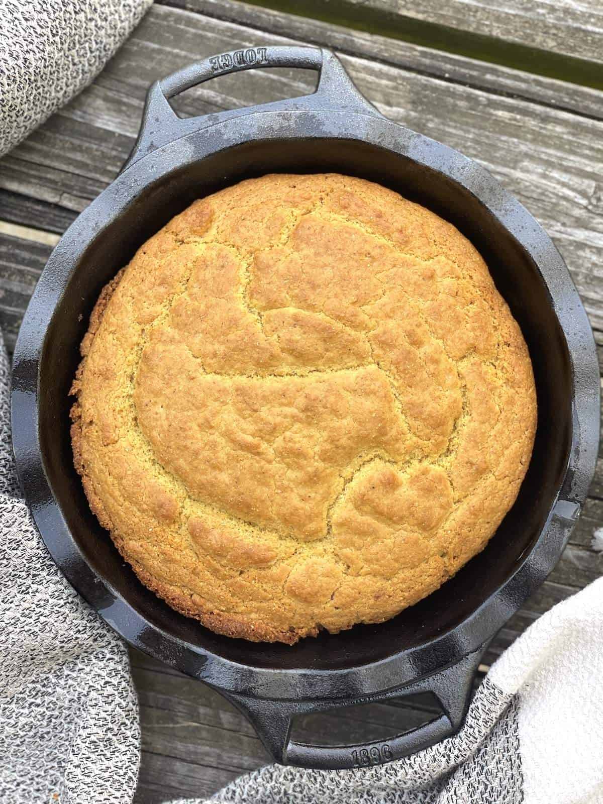 A cast iron pie pan with baked golden brown southern cornbread in it.