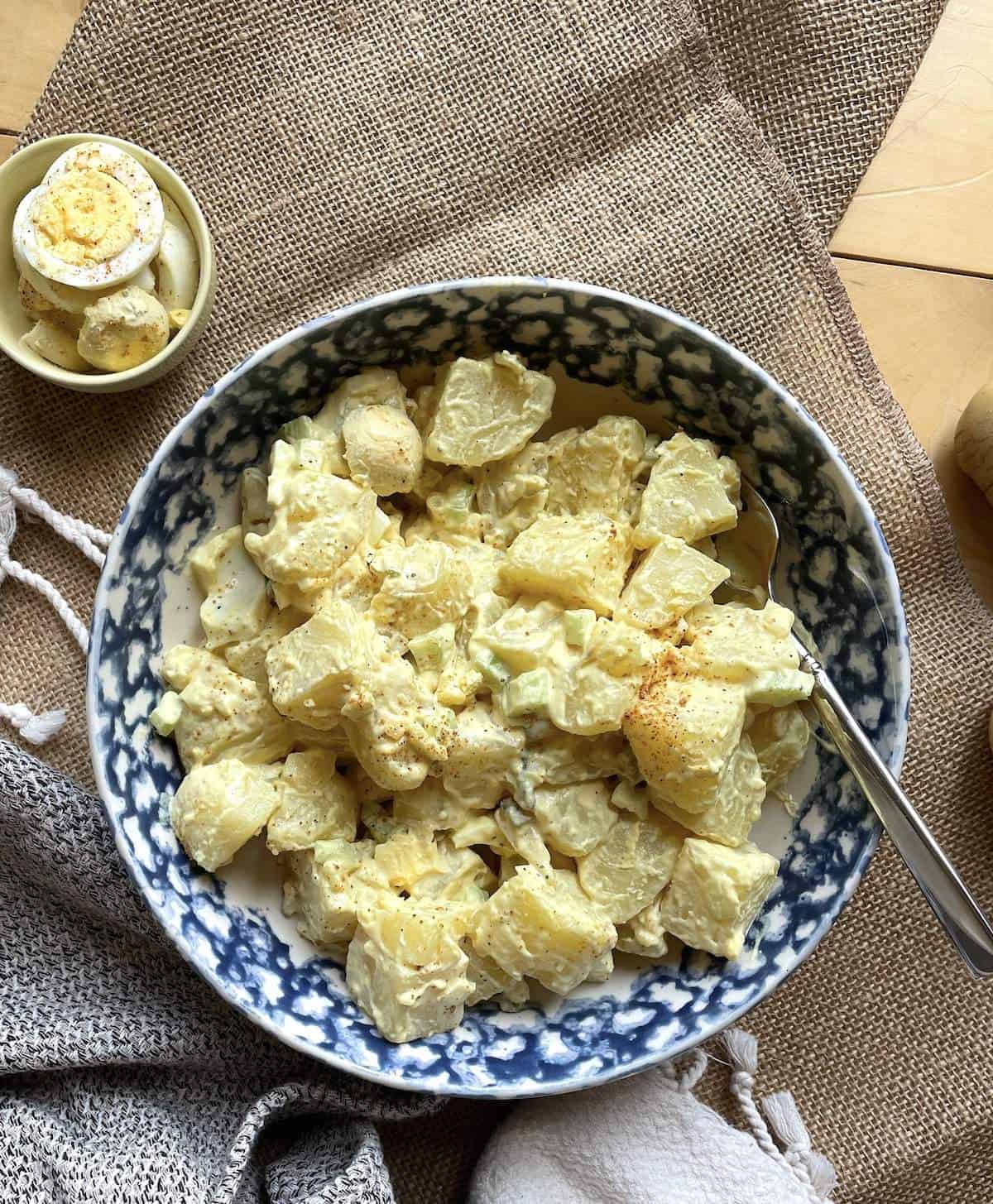 A bowl of southern potato salad with mustard dressing and hard-boiled eggs on the side.
