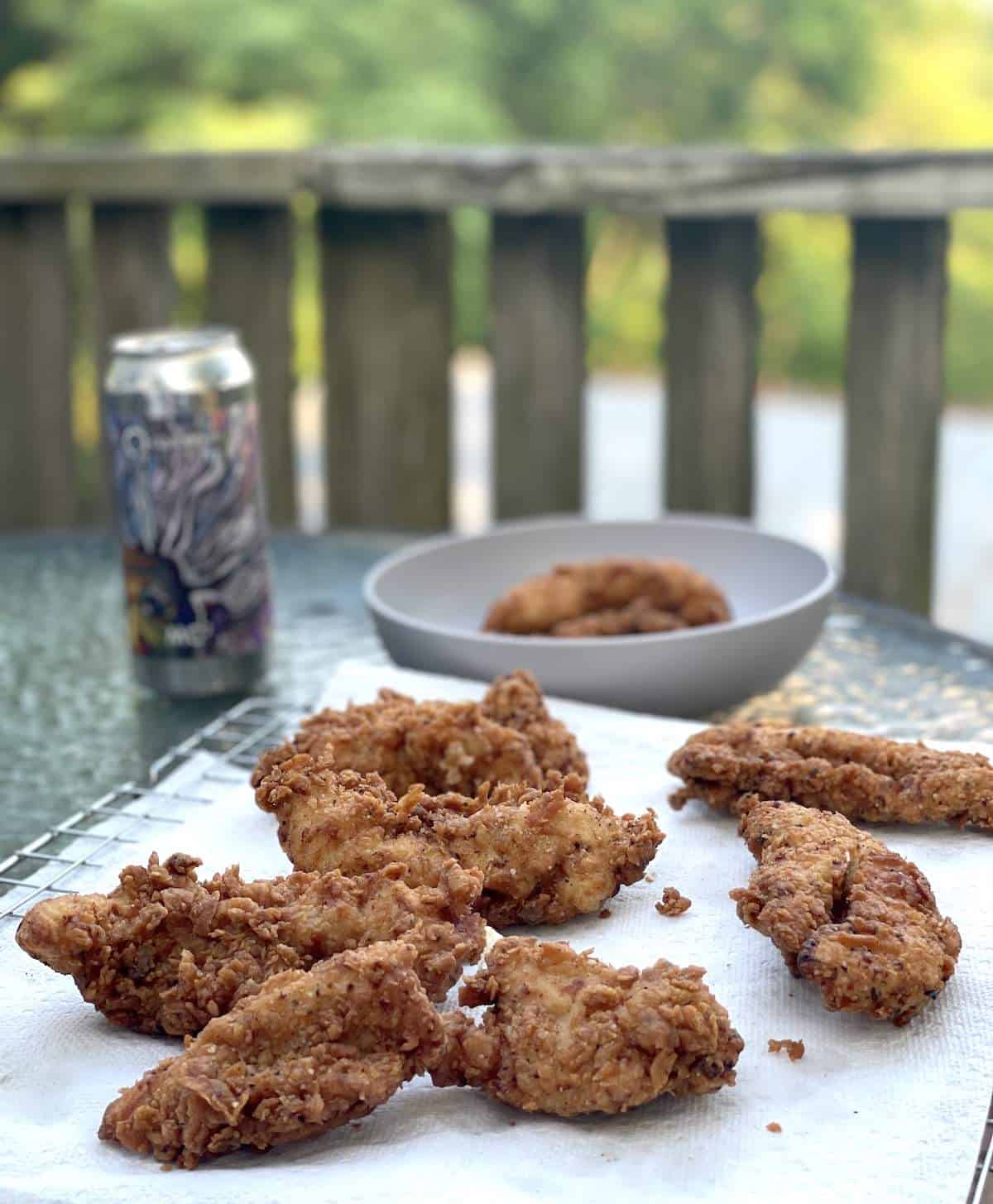 Crispy Fried Chicken Tenders on a paper towel with a beer and a landscape in the background.