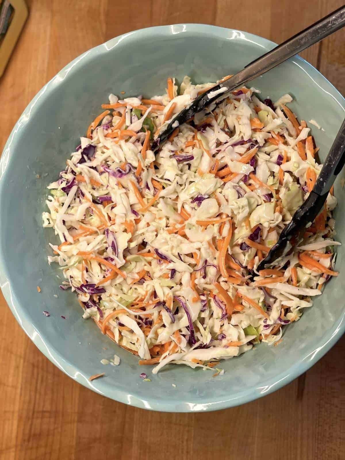 A bowl of shredded cabbage and carrots coated in coleslaw dressing.