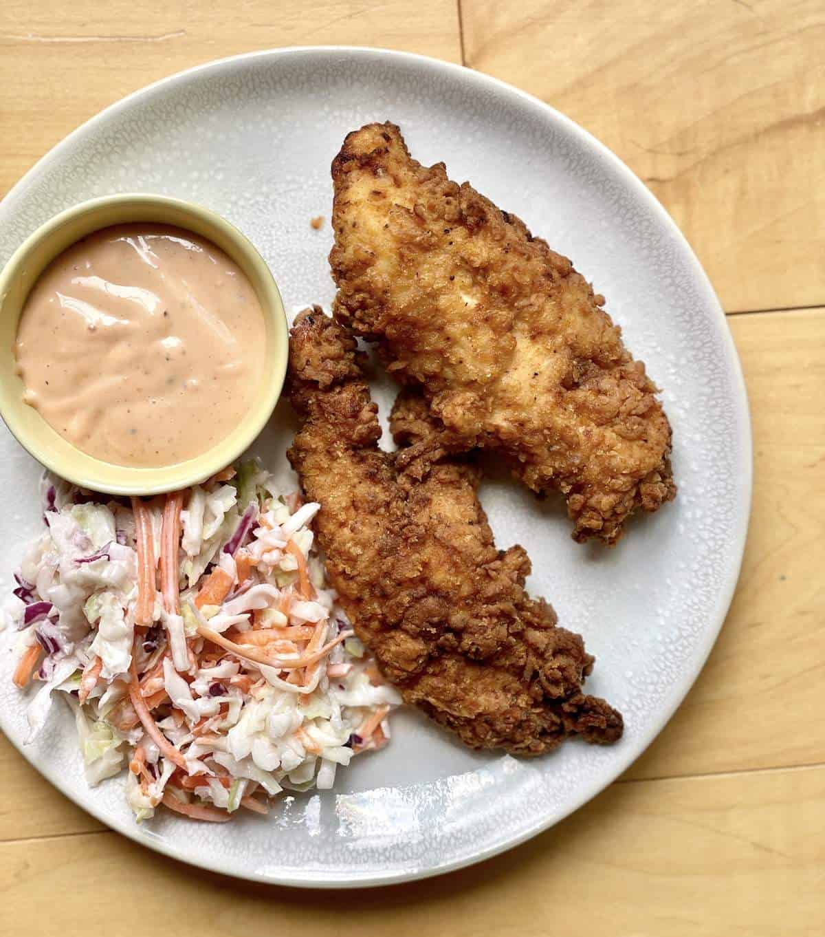 Two homemade raising canes chicken tenders, canes sauce, and canes coleslaw on a white plate.