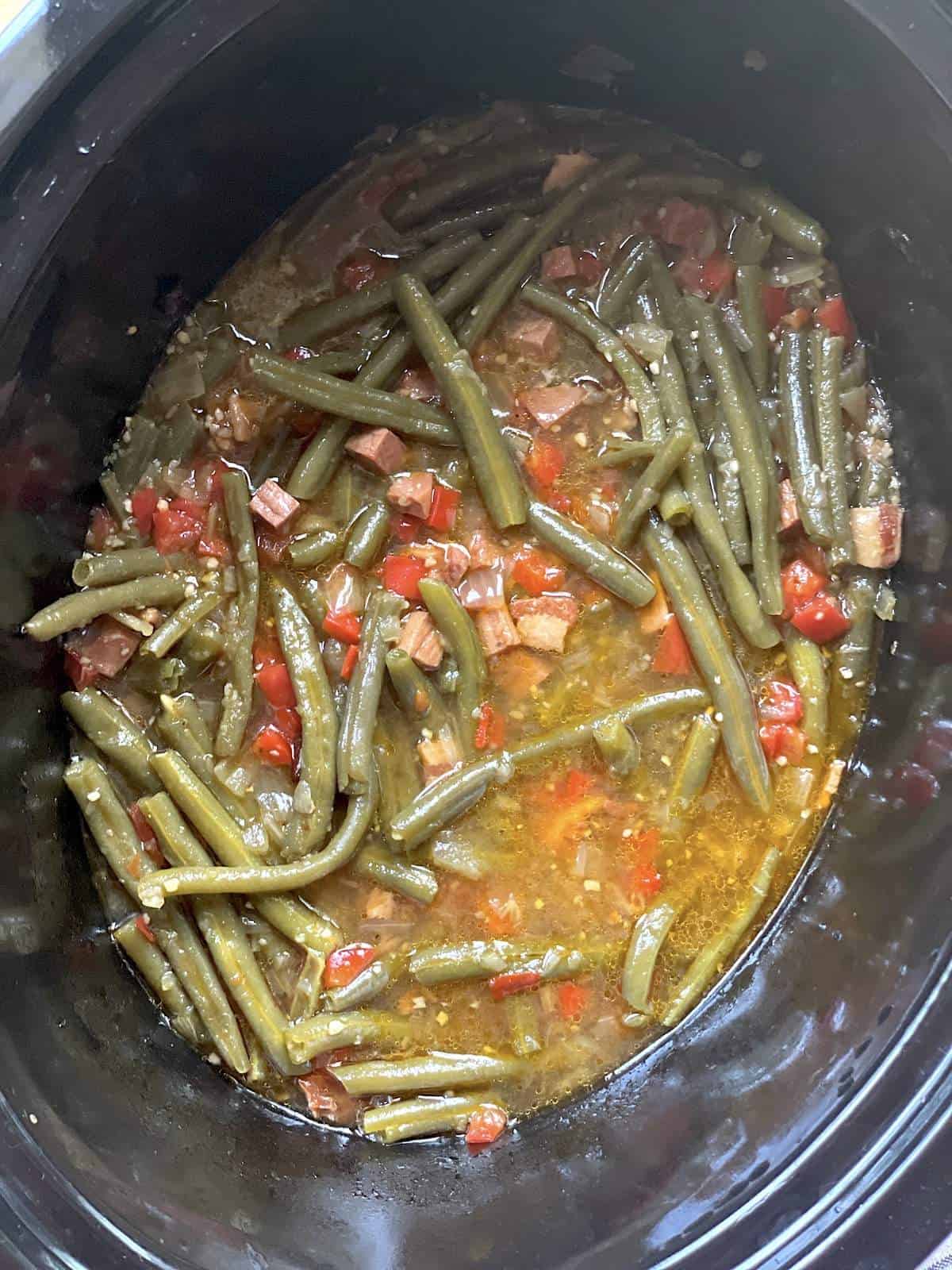 Green beans in a crock pot that have cooked down with bacon and ham.