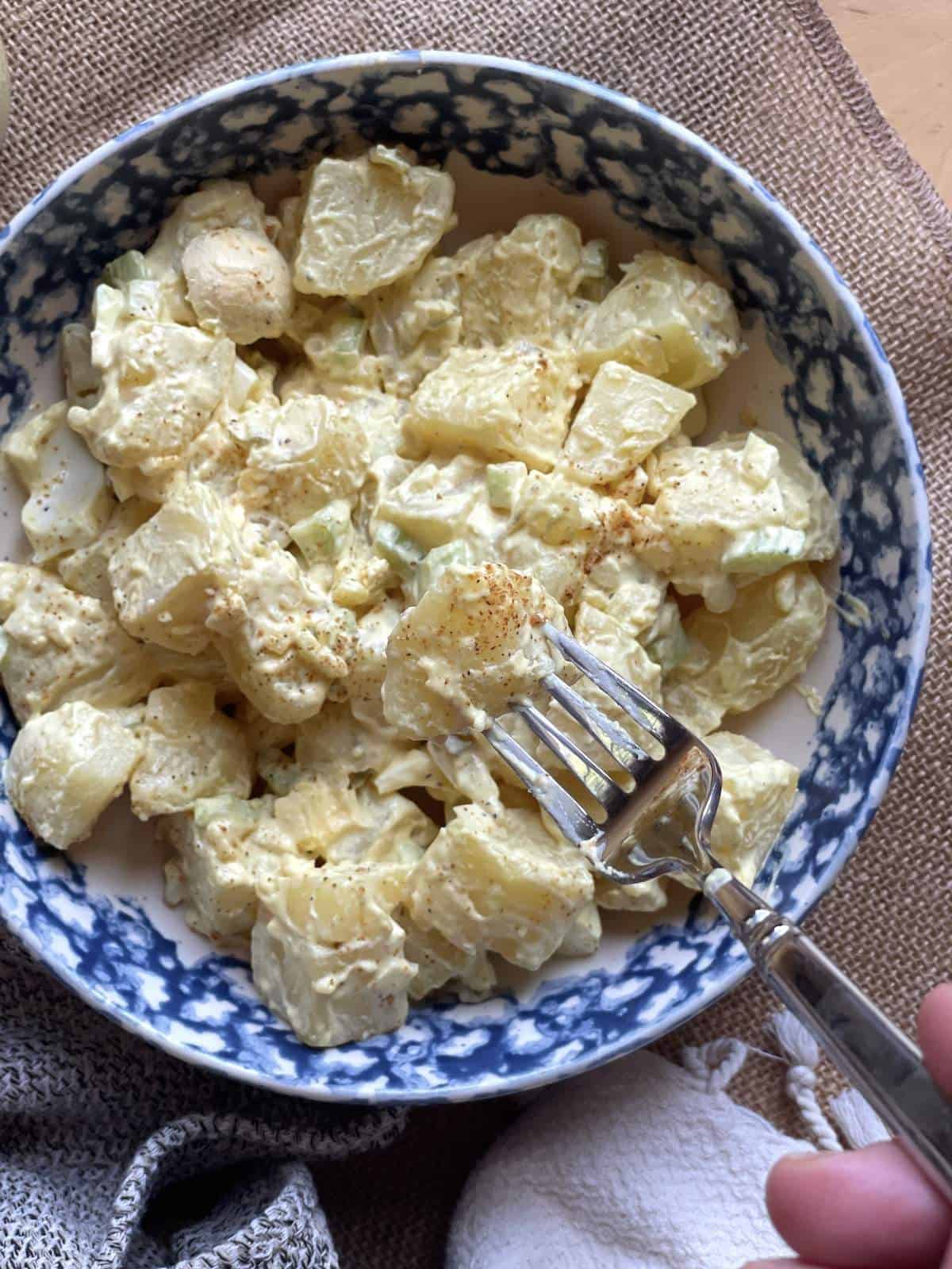A bowl of southern potato salad topped with a pinch of creole seasoning.