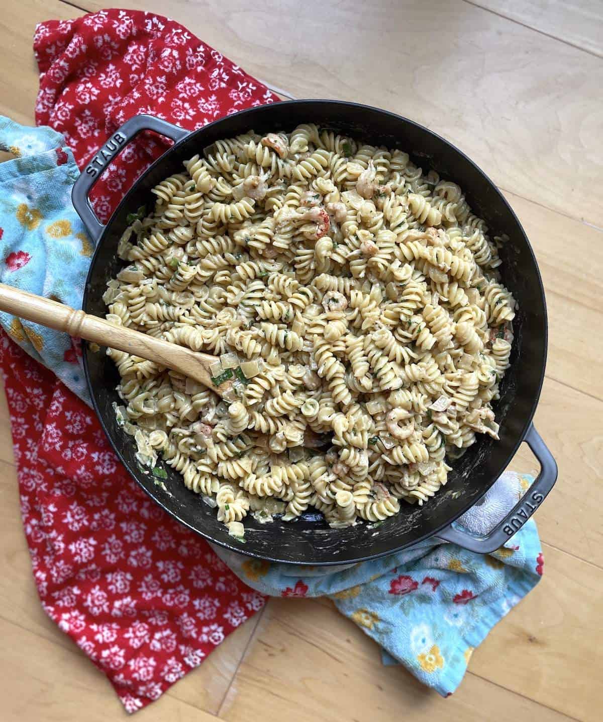 Crawfish Monica in a large skillet with a wooden spoon and two towels.