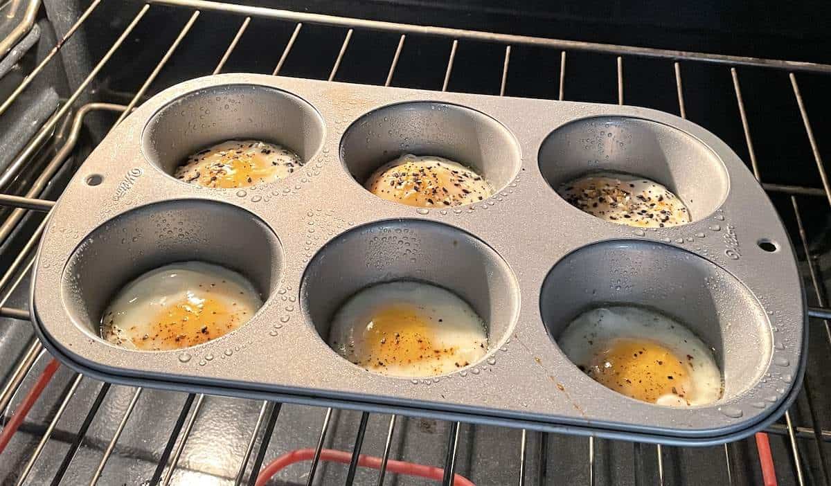 A muffin tin in the oven with eggs baking in the individual cups.