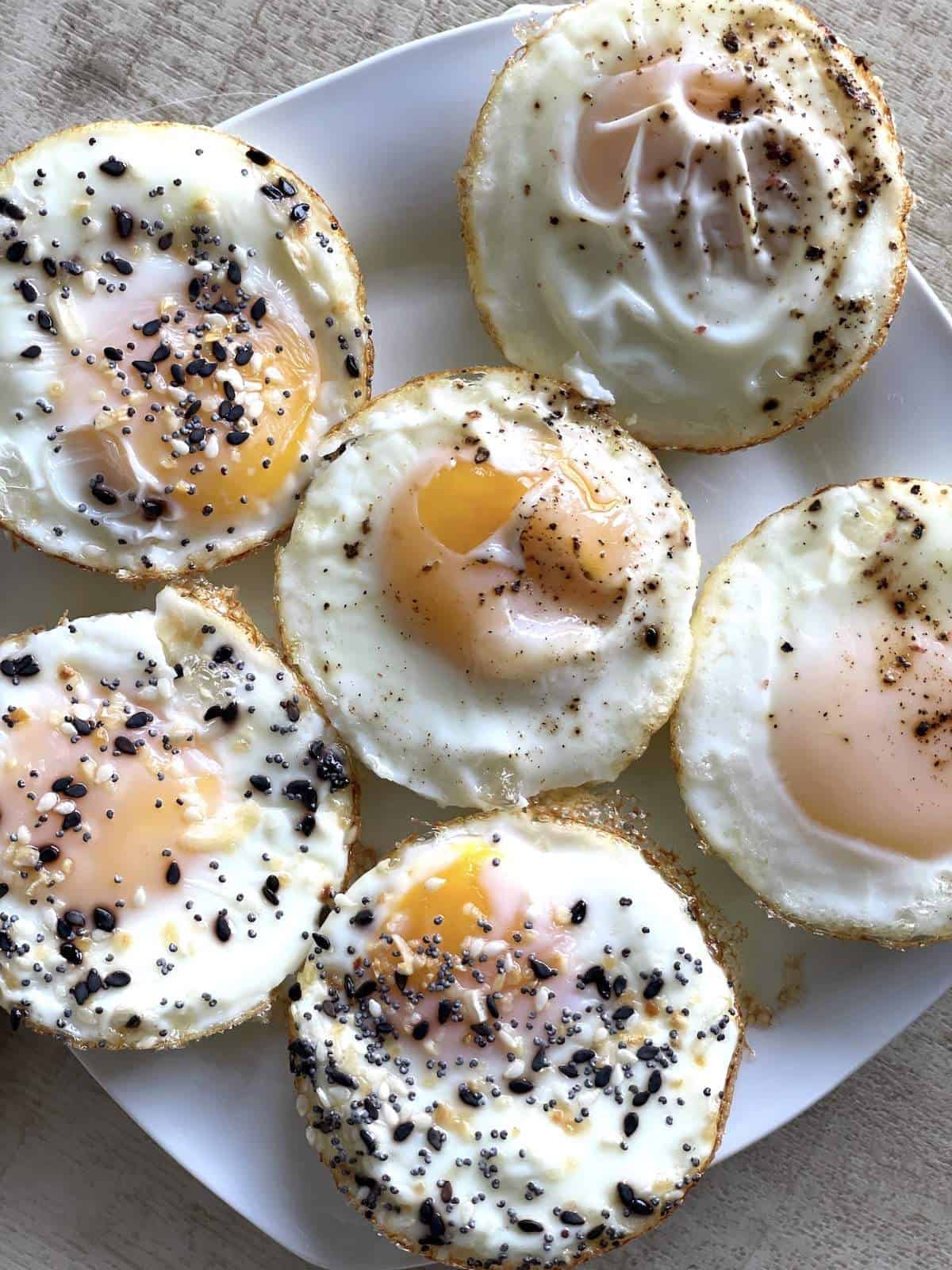 Soft-boiled baked eggs on a white plate with everything bagel seasoning on them.