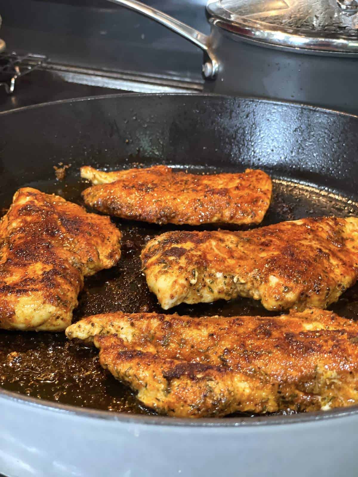 Chicken breasts cooking in a cast iron skillet.