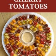 A pin image of a dehydrator tray covered in sliced cherry tomatoes.