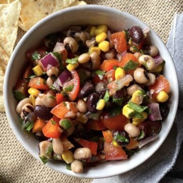A small bowl of redneck caviar with black-eyed peas, corn, black beans, and tomatoes with a side of tortilla chips.