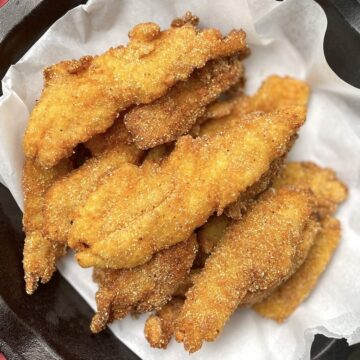 A cast iron pan with parchment paper topped with fried catfish fillets.