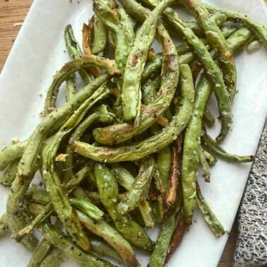 Seasoned air fried green beans on a white plate.
