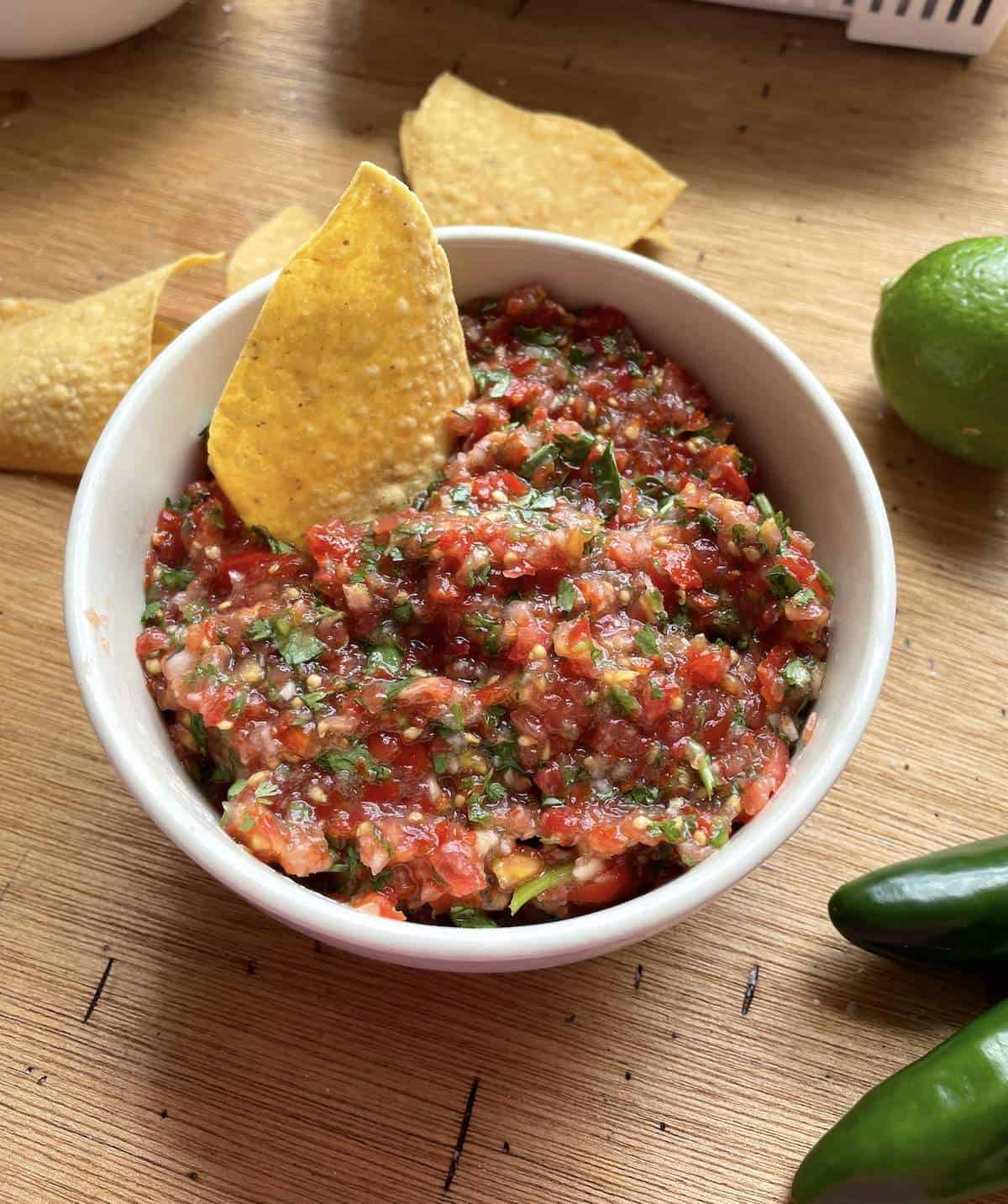 A bowl of cherry tomato salsa with a tortilla chip sticking out of it.