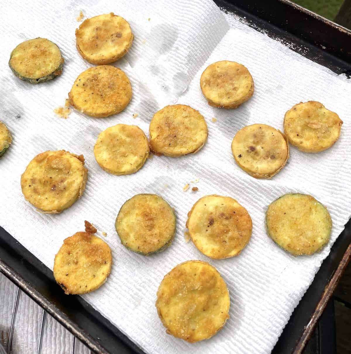 Fried squash and zucchini slices draining on a paper towel on a cookie sheet.