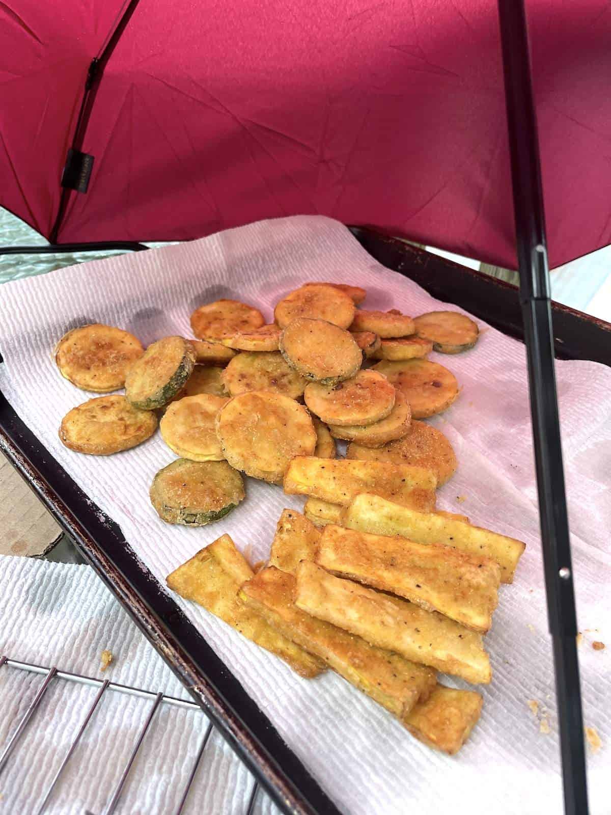 Fried squash slices and strips on a paper towel with an umbrella covering them.