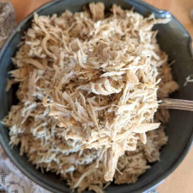 A big bowl of instant pot shredded chicken being served with a spoon.